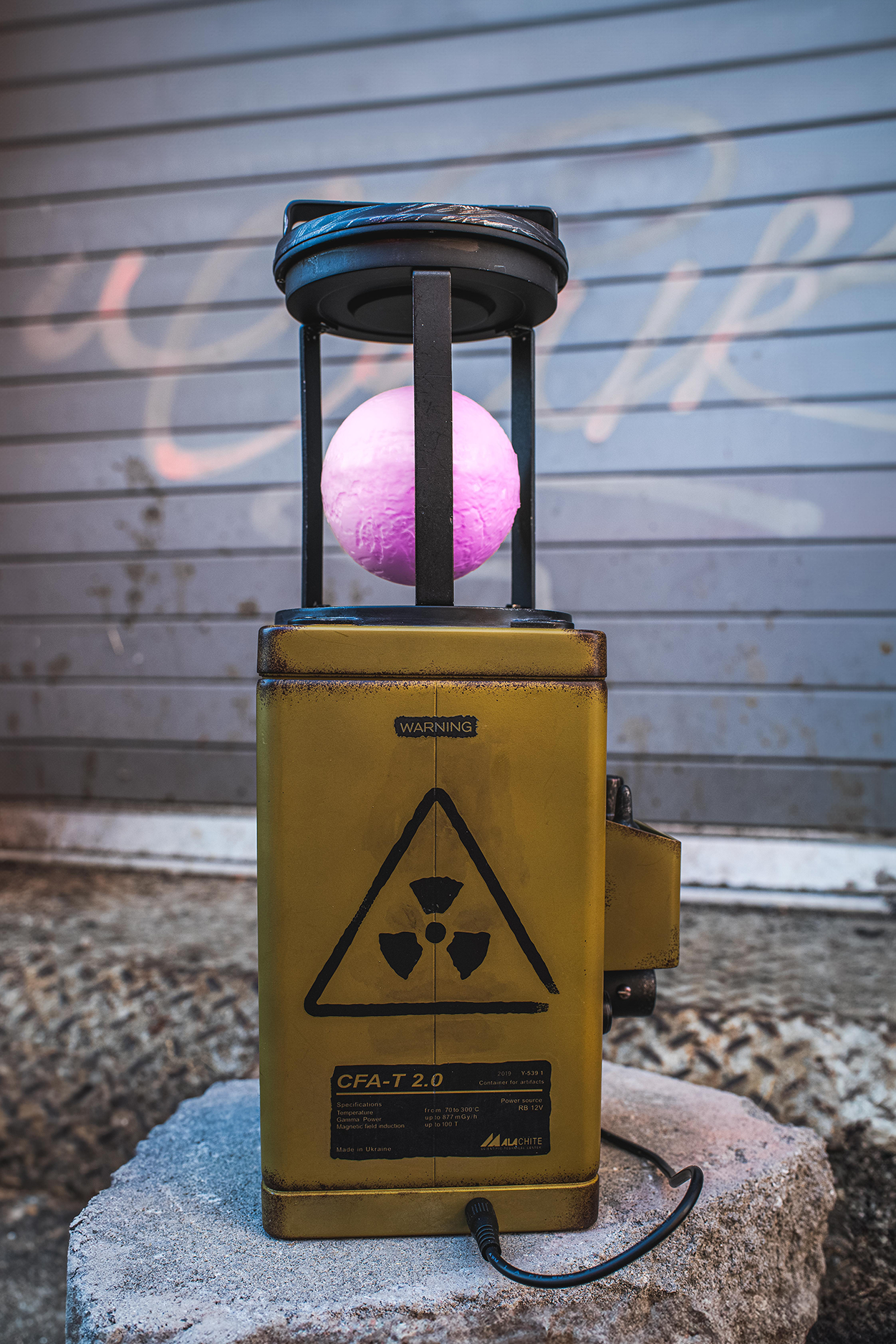 Yellow radiation warning device with a pink sphere on top against a graffiti-covered wall.