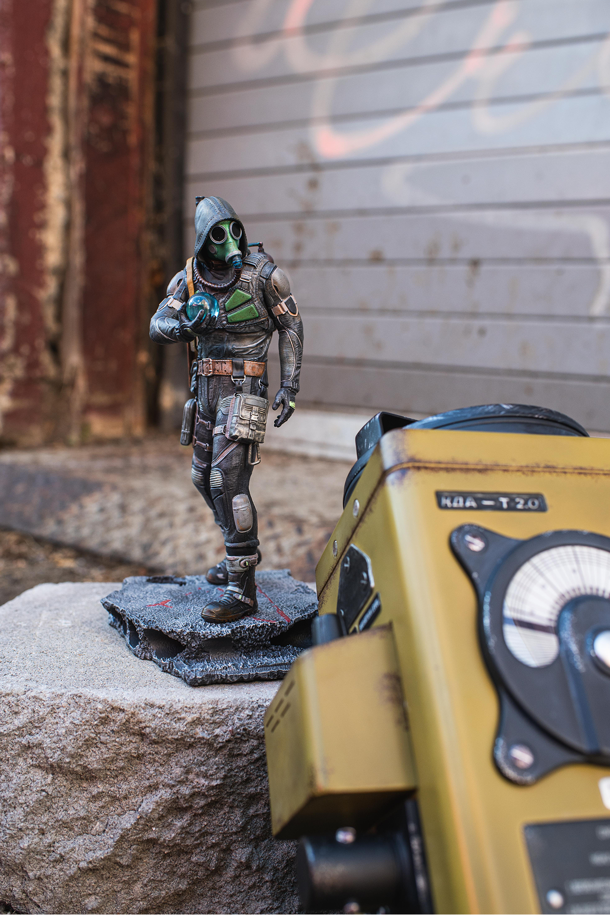 Statue of a character in futuristic gear next to a yellow and black device on a stone surface.