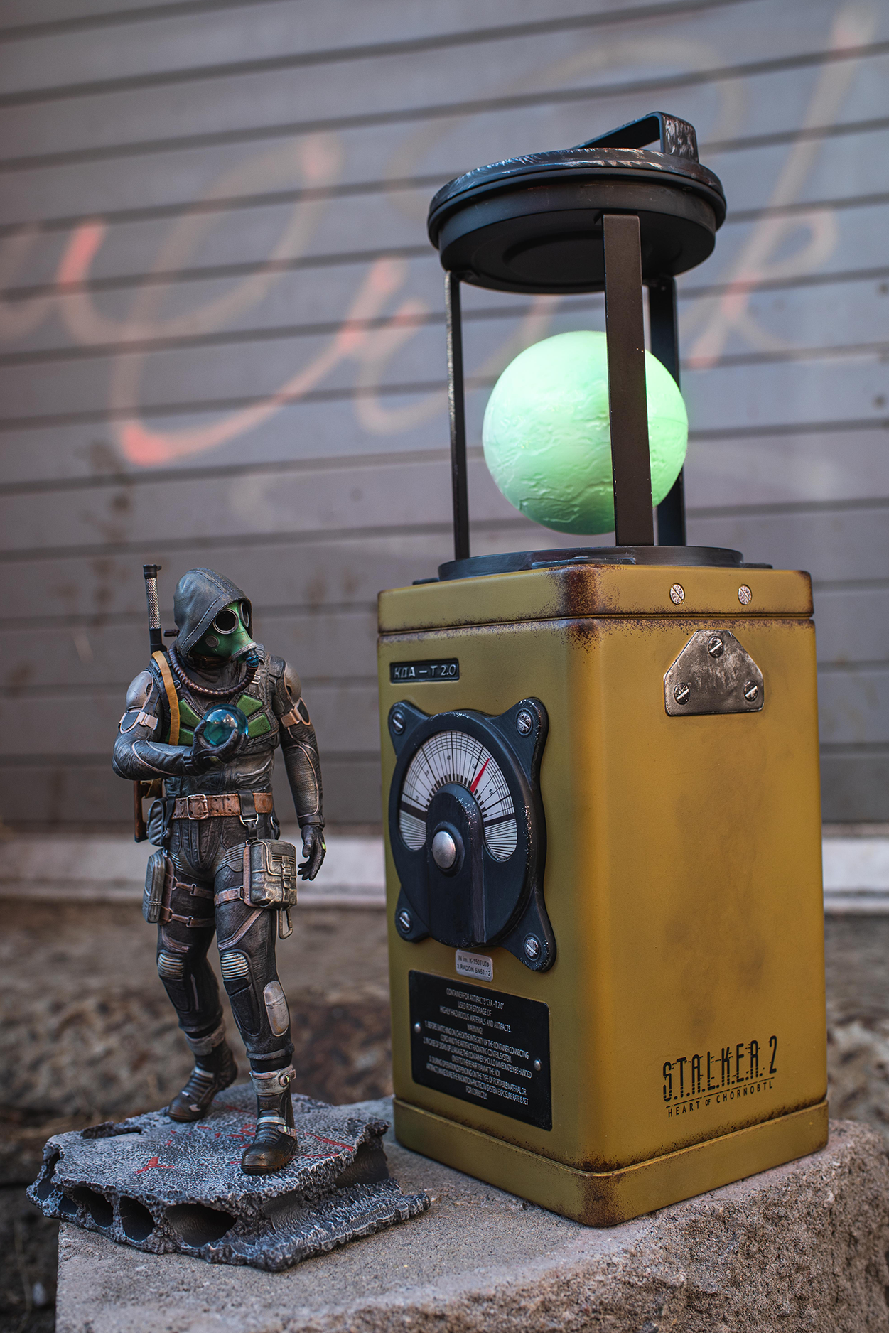 Statue of a character from a video game next to a yellow cylindrical object with a green light on a concrete surface.